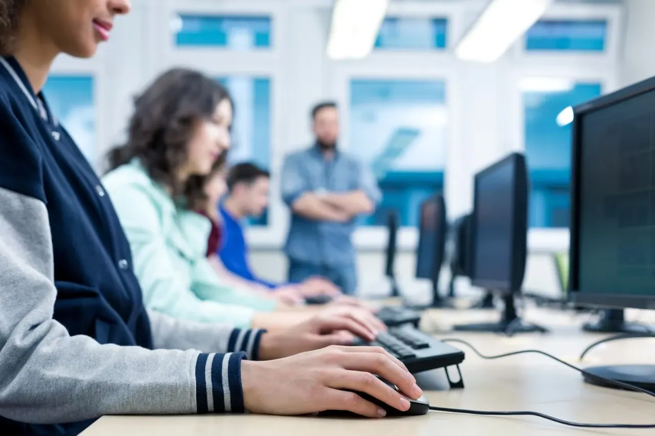 Students follow a computer training course, with a trainer in the background