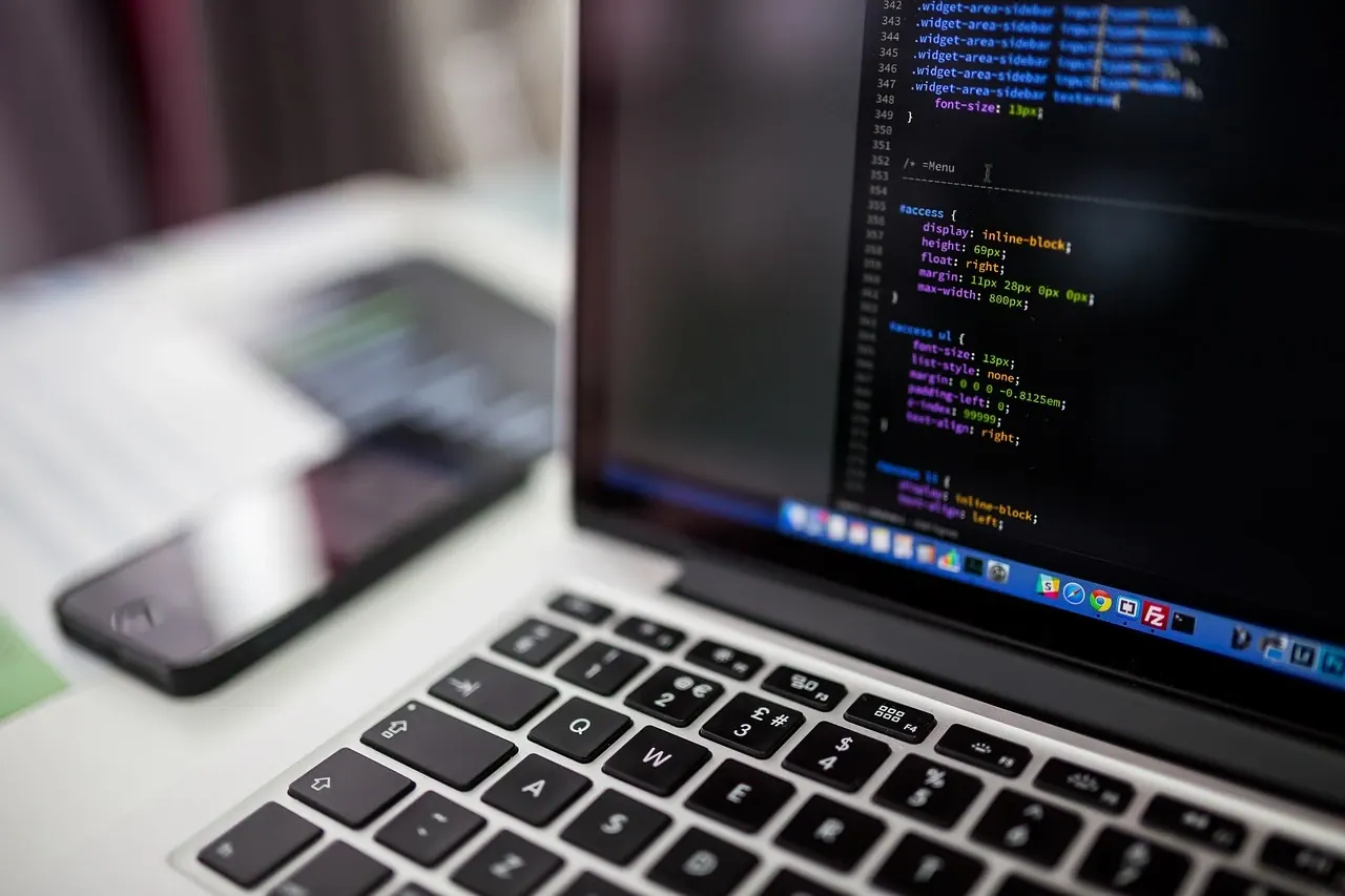 Laptop showing web development code, with a smartphone in the background